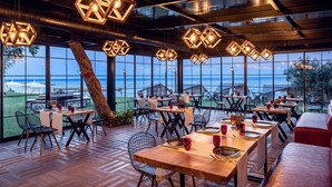 A restaurant with hexagonal pendant lights, wooden tables, and chairs, overlooking a scenic view of the sea. - Rixos Beldibi - Adult Only - The Land of Legends Access (Kemer)