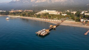 Un hotel frente al mar con un muelle que se adentra en el agua, con acceso a la playa y vistas a las montañas al fondo.
