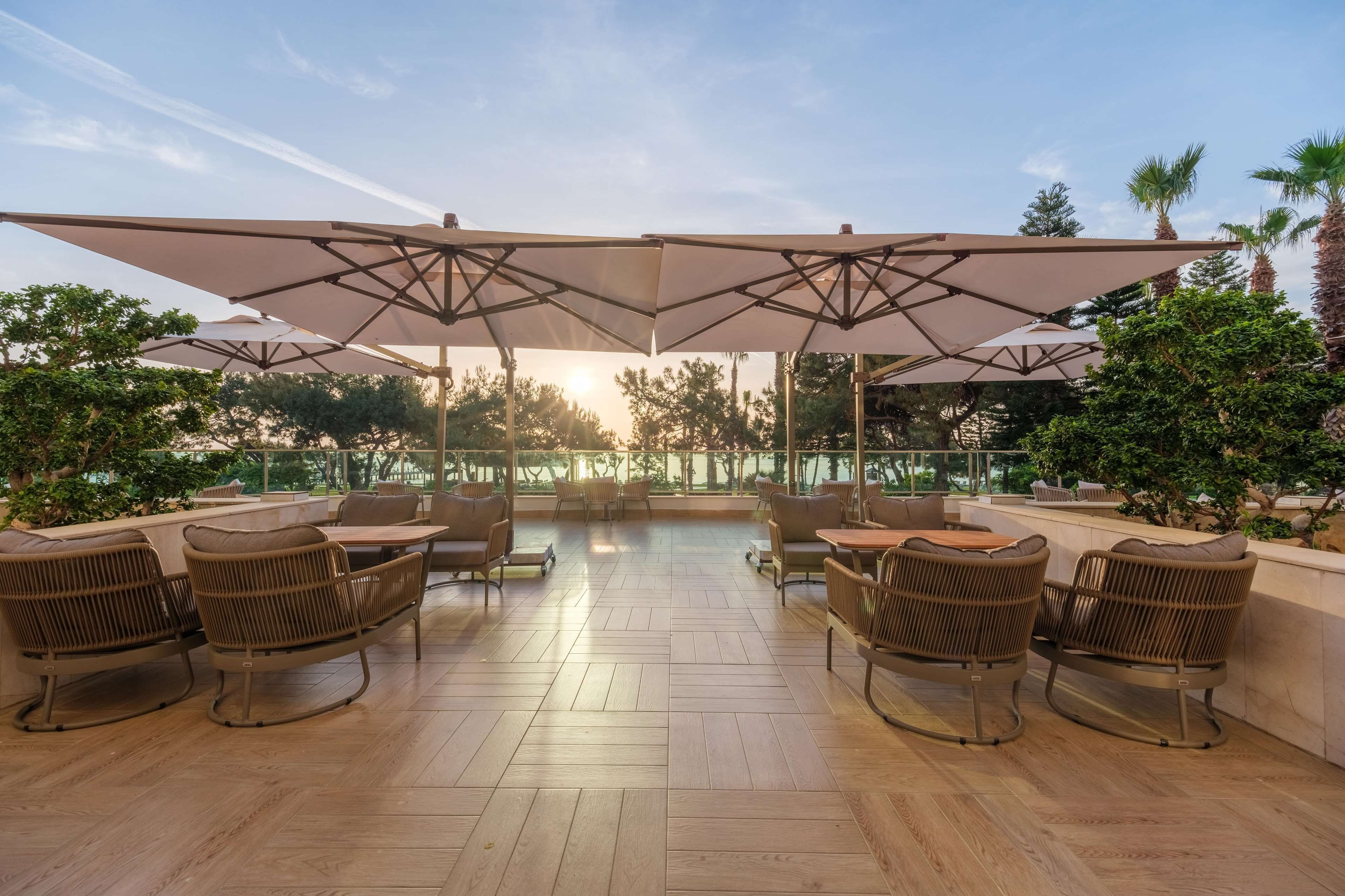 An outdoor patio with wooden flooring, wicker furniture, and large umbrellas providing shade.