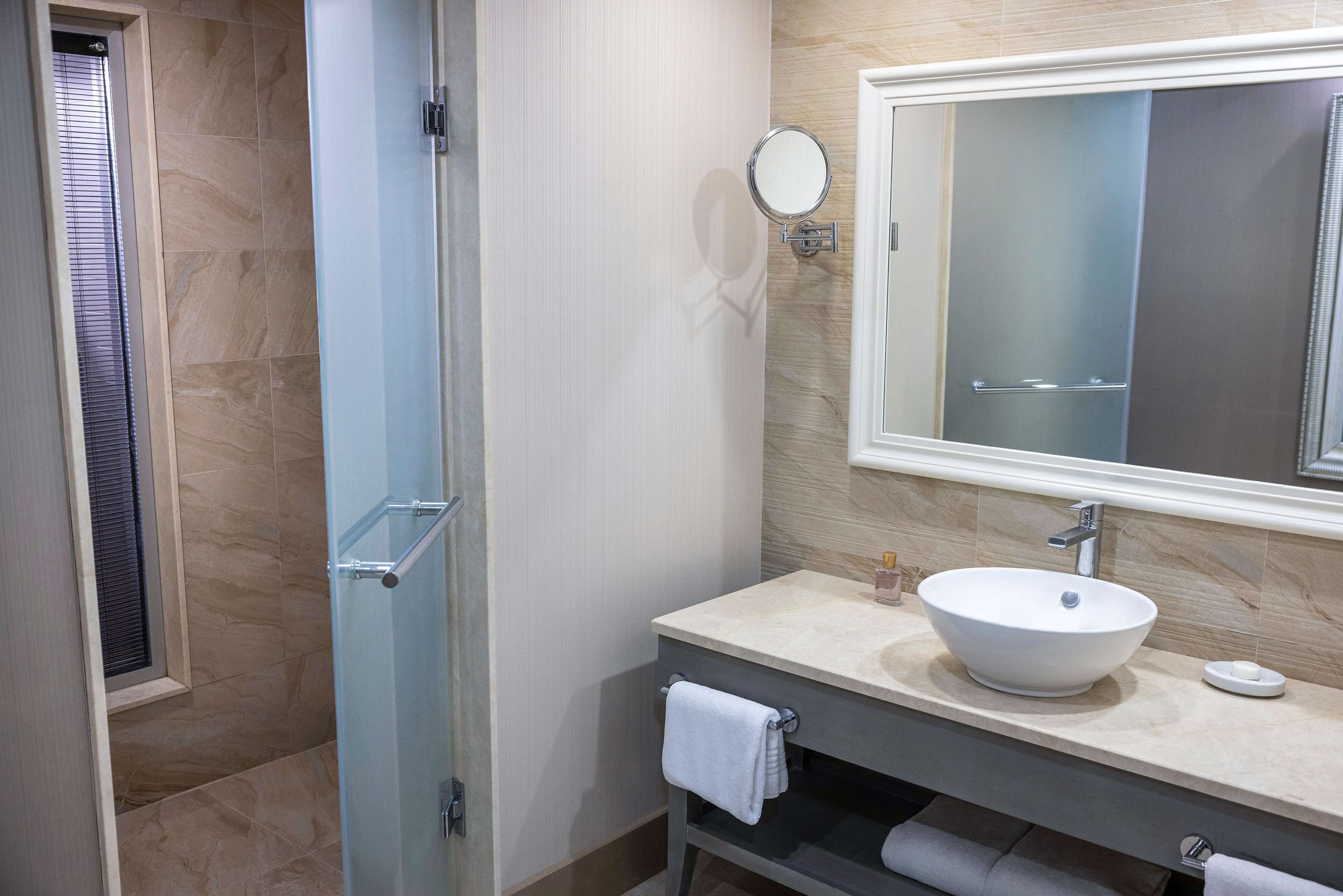 A modern bathroom with a glass shower enclosure, a large mirror, and a beige sink with a vessel basin.