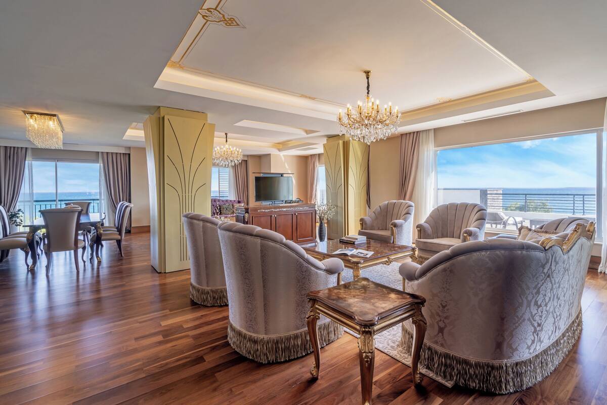 A spacious living room with a large window, elegant furniture, and a chandelier.