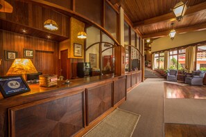 Ein Empfangsbereich mit einem Holzbüro, gerahmten Bildern, einem Coca-Cola-Schild und einer Treppe, die zu einem Balkon mit Sitzgelegenheiten im Freien führt.