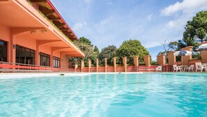 Une piscine à l’eau d’un bleu cristallin, entourée d’un bâtiment à la façade rouge et de chaises blanches disposées le long du bord de la piscine.
