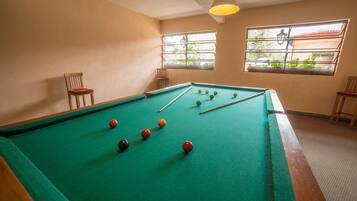 A pool table with balls, two chairs, and windows with a view of greenery.