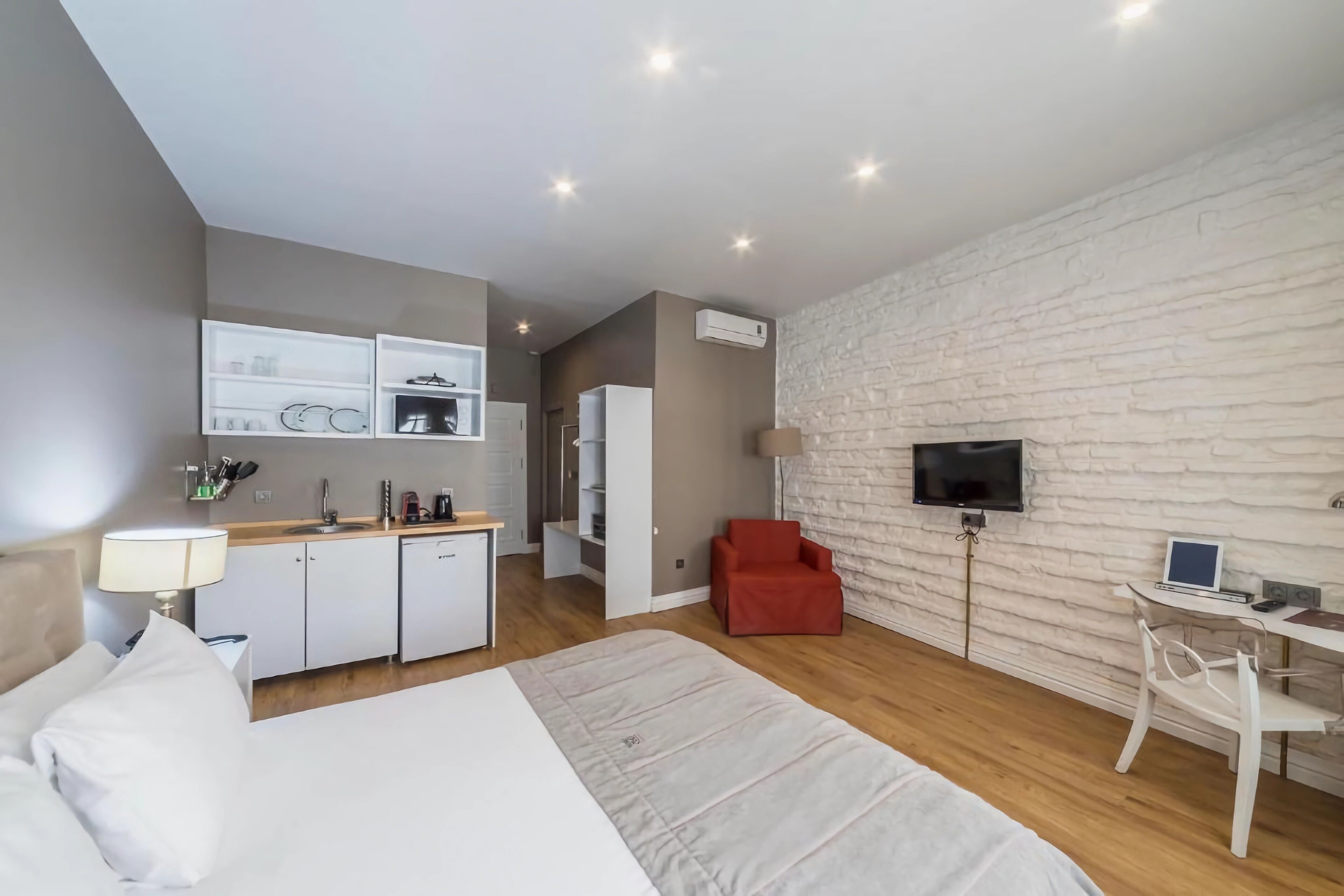 Une chambre d’hôtel moderne équipée d’un lit, d’un bureau avec un ordinateur, d’une télévision et d’une kitchenette.