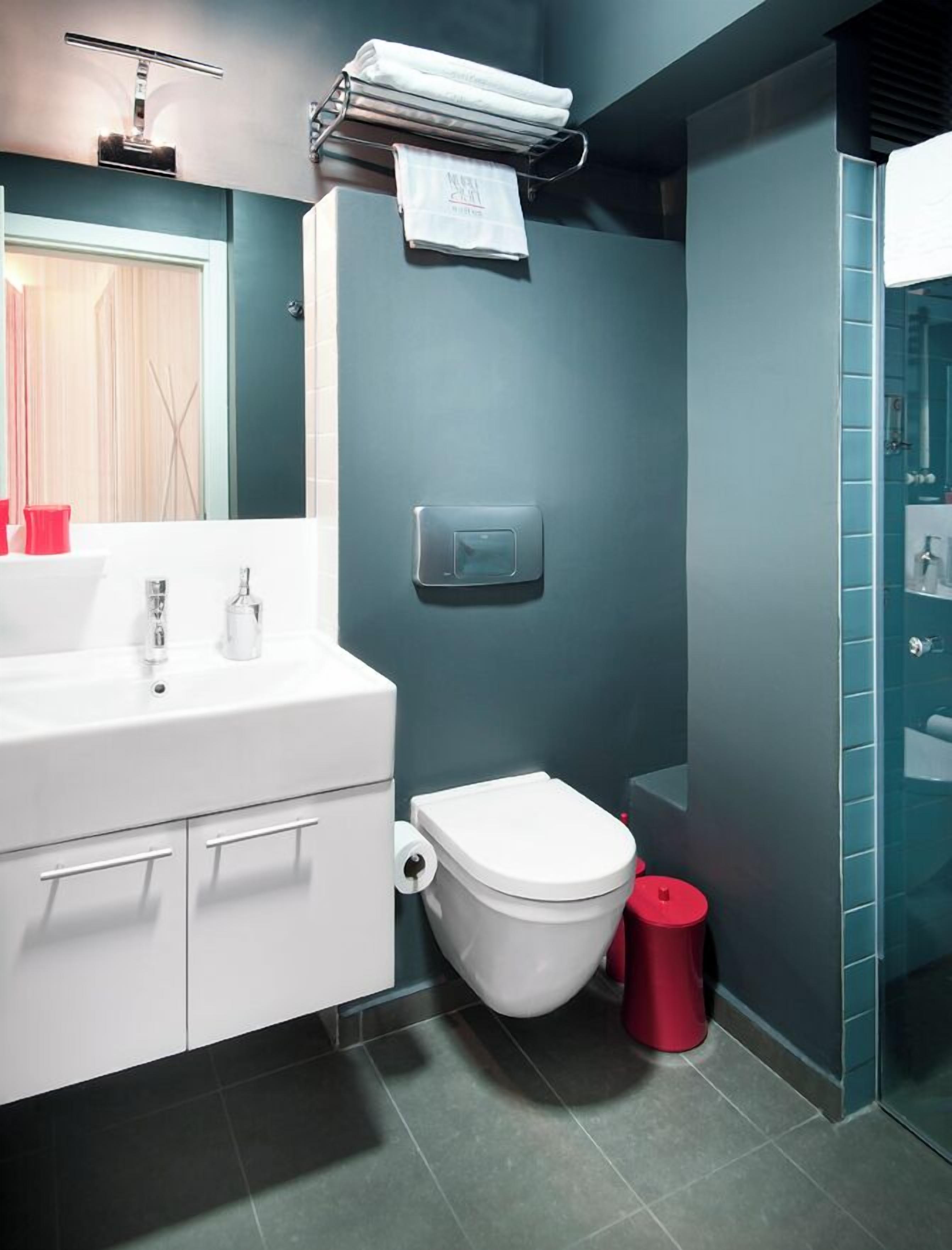 Ein modernes Badezimmer mit einem weißen Waschtisch, einer Toilette, einer roten Mülltonne und einer Duschkabine aus Glas.