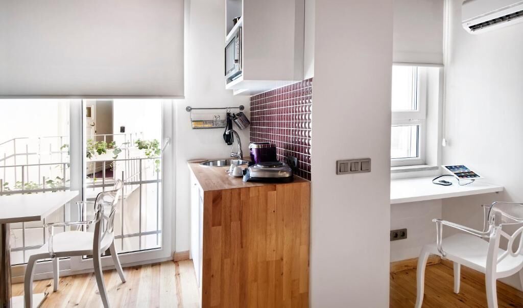 A modern kitchen with a wooden countertop, a built-in microwave, and a window overlooking a balcony.