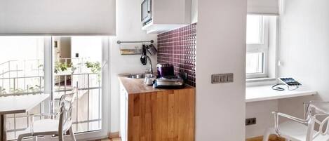 A modern kitchen with a wooden countertop, a built-in microwave, and a window overlooking a balcony.