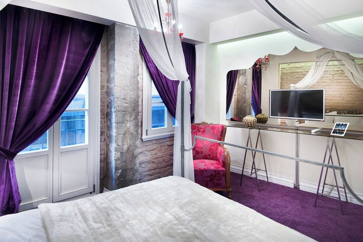 Una habitación de hotel con cama, escritorio, computadora, silla y cortinas.
