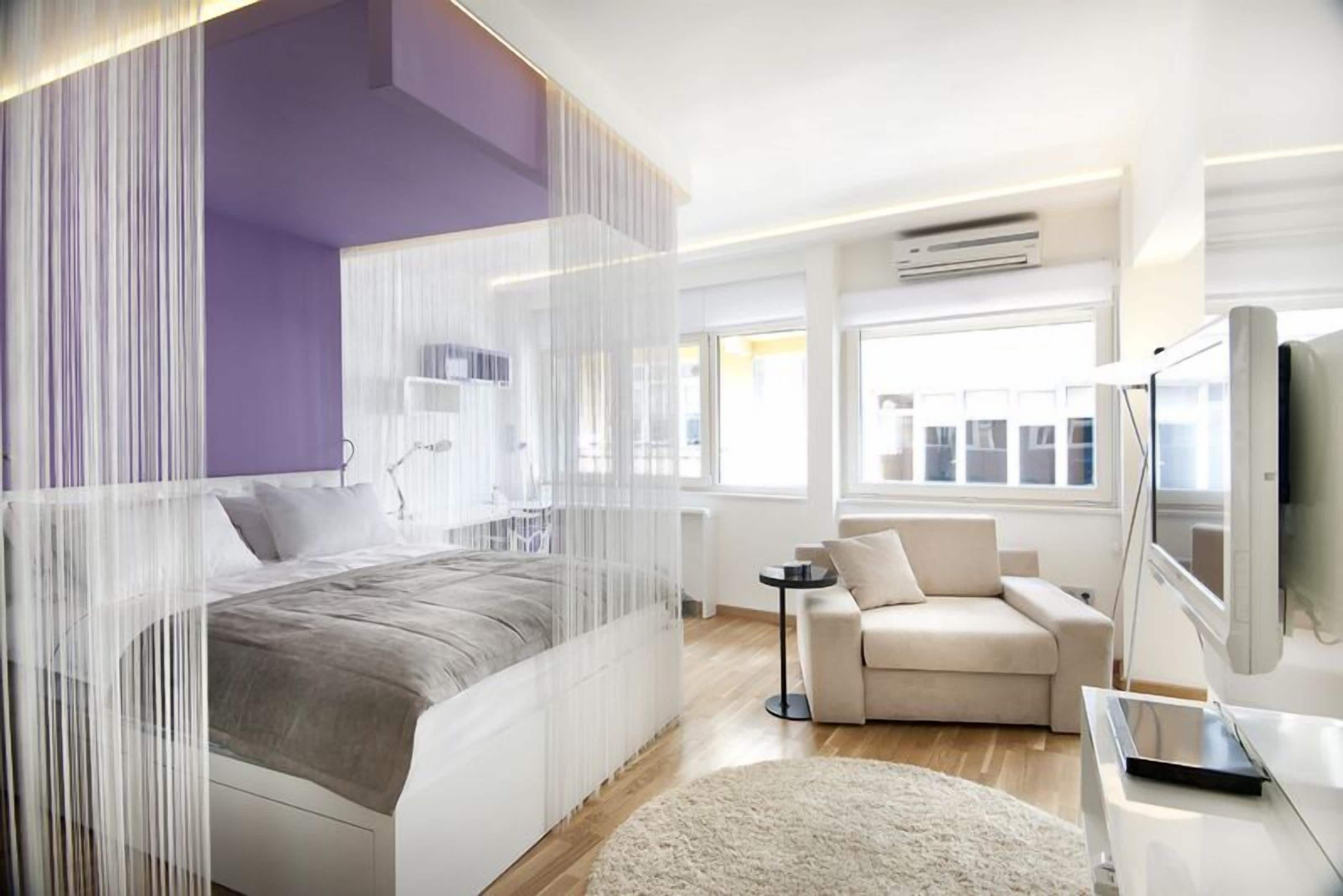 A modern bedroom with a bed, a sofa, a TV, and a window.