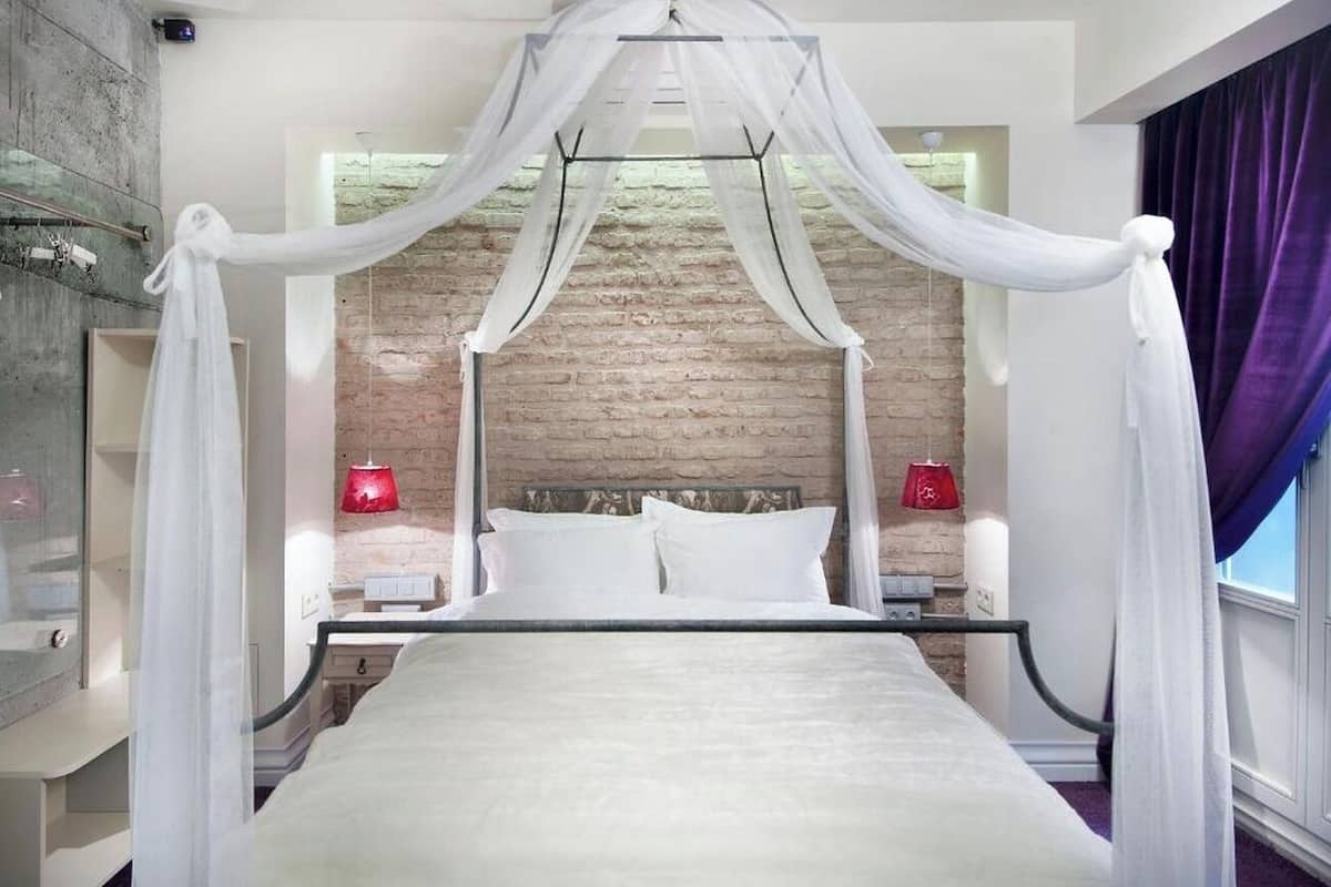 A bedroom with a four-poster bed, a brick wall, and a window with curtains.