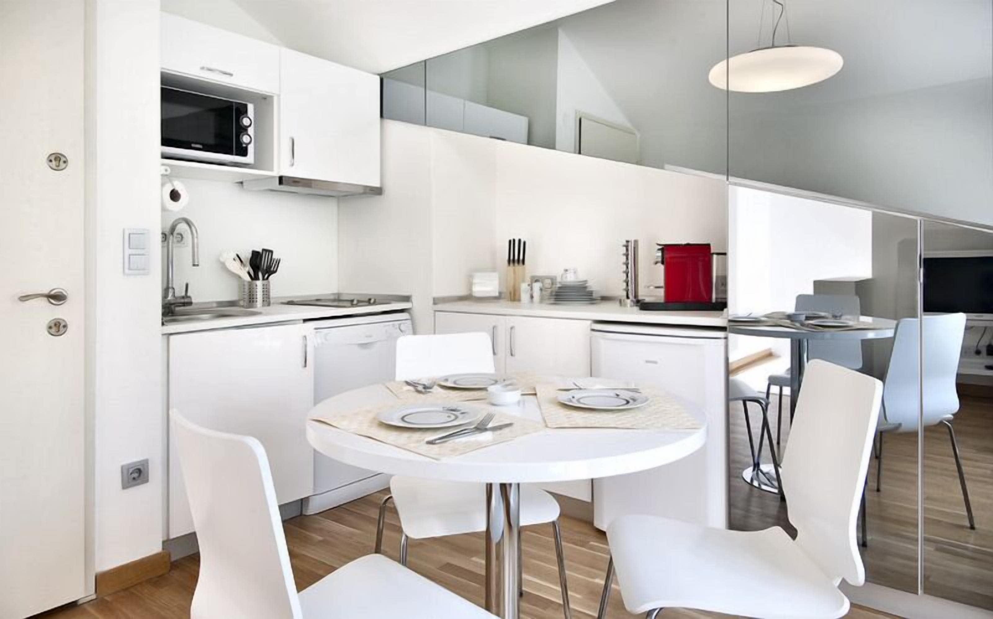 A modern kitchen with white cabinetry, a dining area with a round table, and a red appliance.