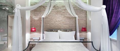 A four-poster bed with white bedding, a brick wall backdrop, and red bedside lamps.