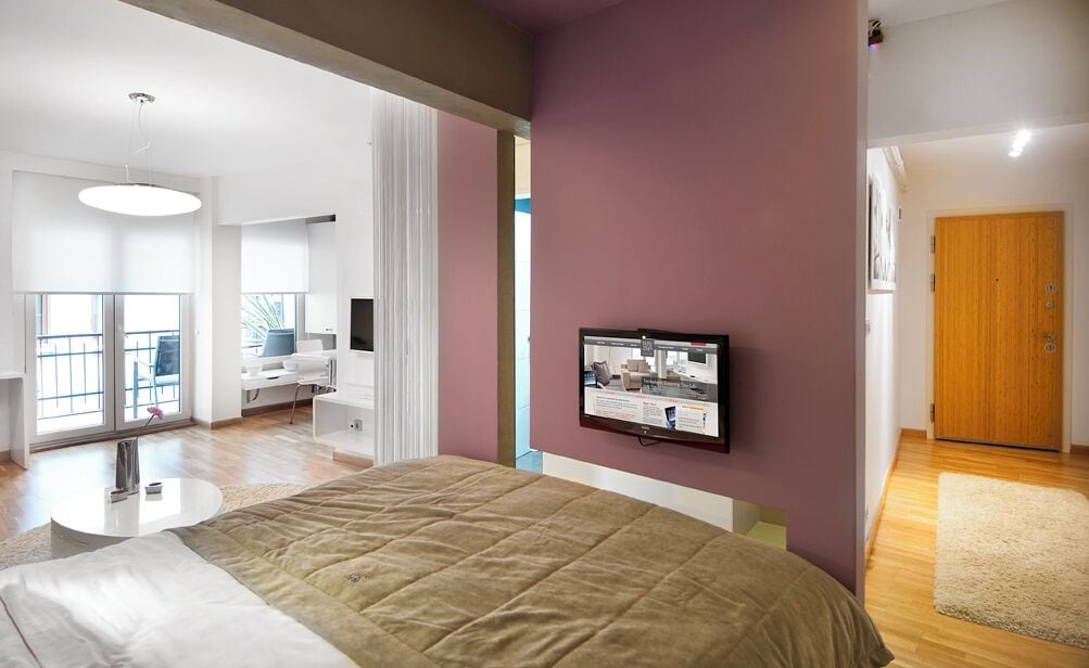Ein modernes Schlafzimmer mit einem großen Bett, einem an der Wand befestigten Fernseher und einer Holztür.