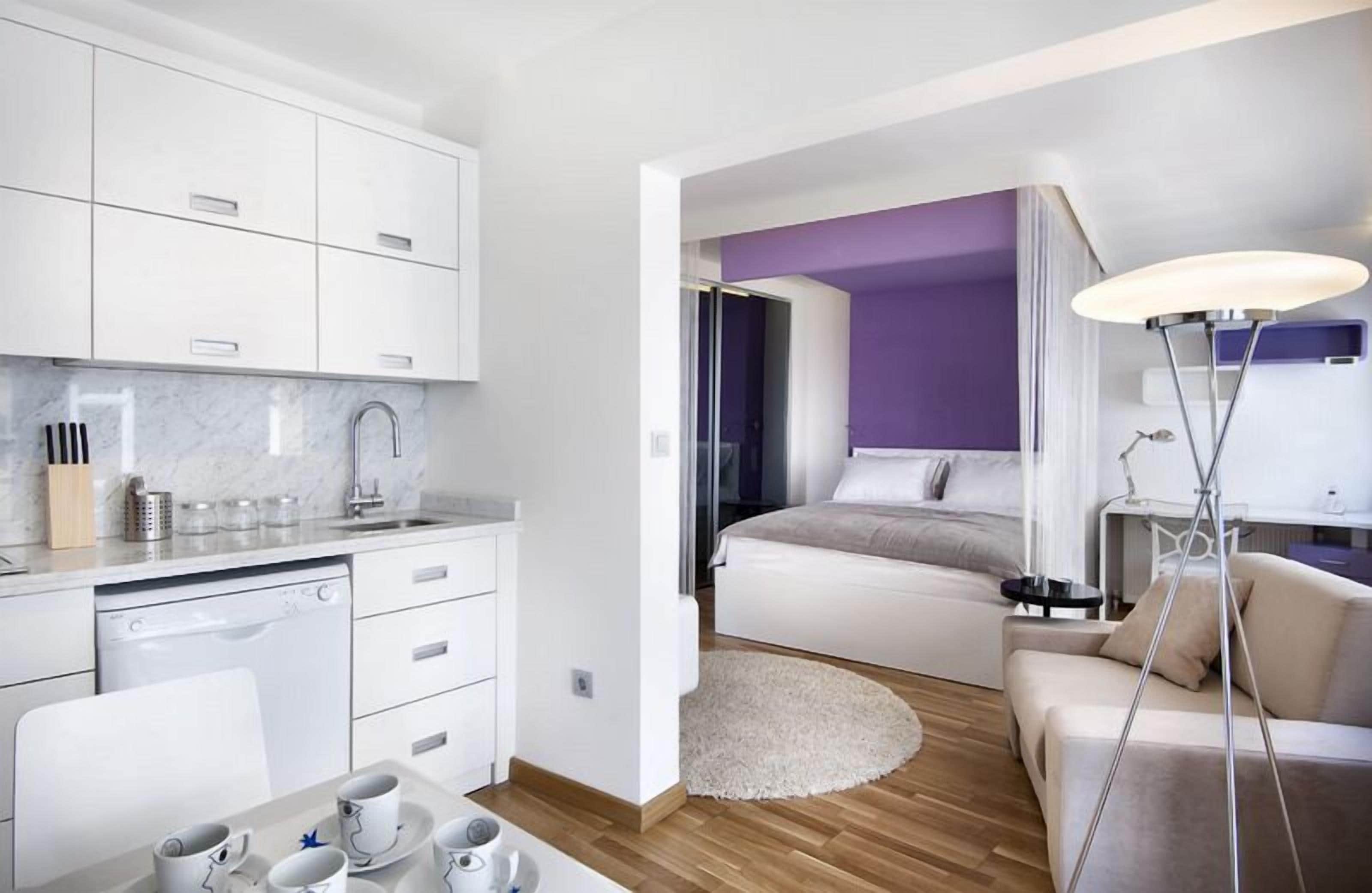 A modern hotel room with a kitchen, a dining area, a bed, and a living area.