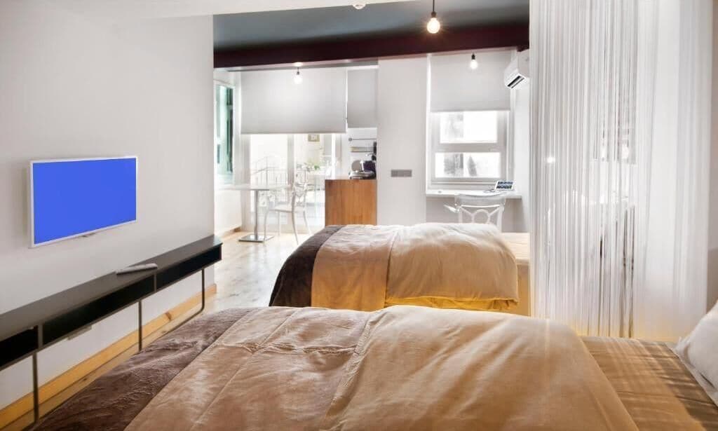 A modern hotel room with a flat-screen TV, two beds, a desk, and a view of the city.