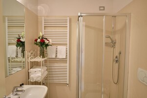 Bagno con doccia vetrata, lavabo, specchio e porta asciugamani con asciugamani piegati.