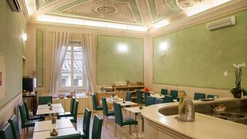 Un espace repas avec des chaises vertes, des tables blanches et une statue décorative posée sur le comptoir.