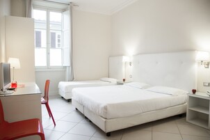 Una camera d'albergo con due letti, una scrivania con una sedia, una lampada e una finestra con tende.