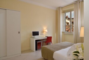 Hotelkamer met een bed, bureau met computer, stoel en raam met gordijnen.