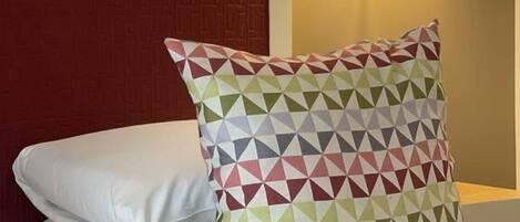 Habitación de hotel con cama, almohada de estampado geométrico, almohada blanca lisa y lámpara fijada a la pared.