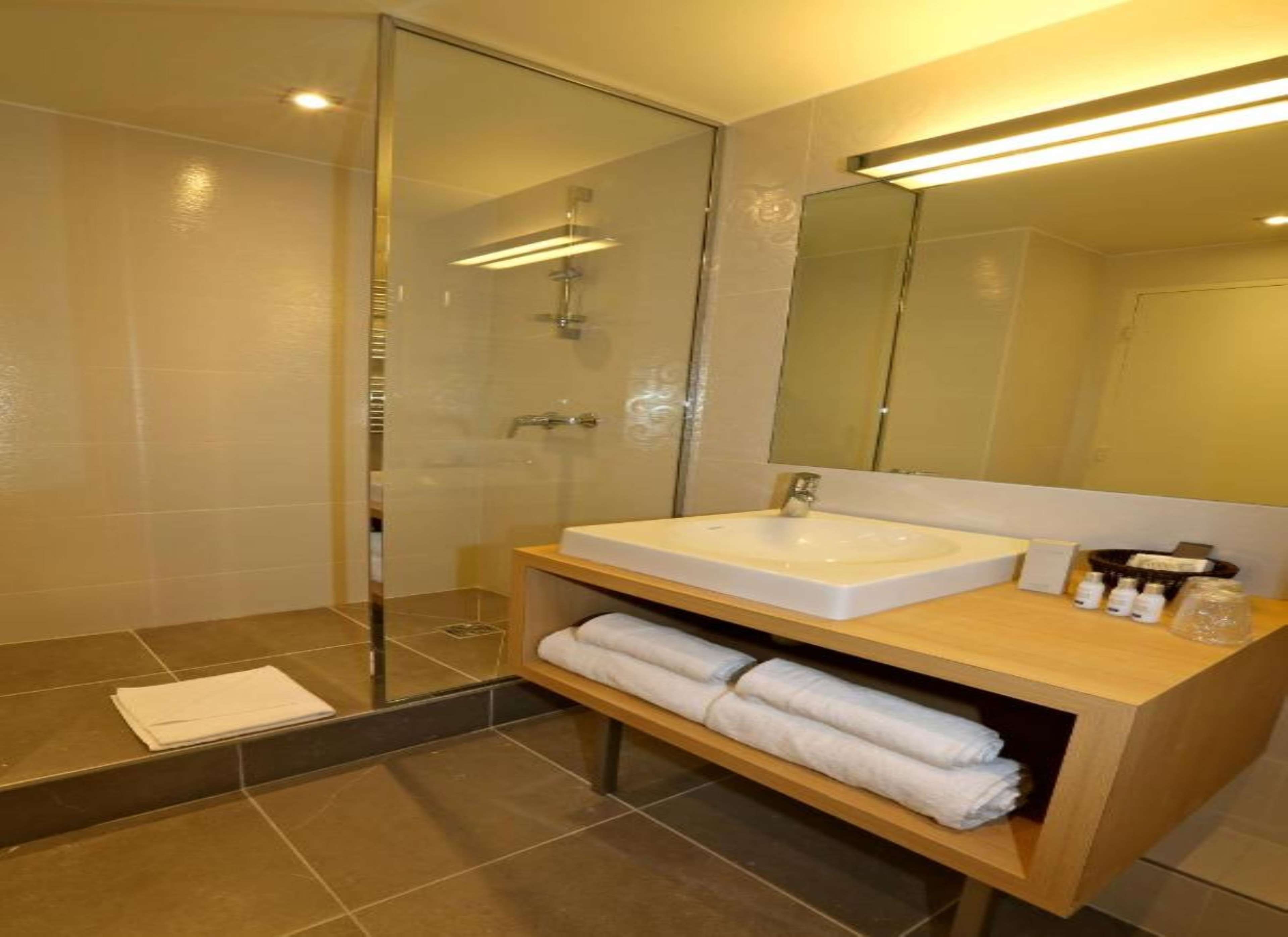 A modern bathroom with a glass shower enclosure, a white sink, and a wooden vanity with towels.