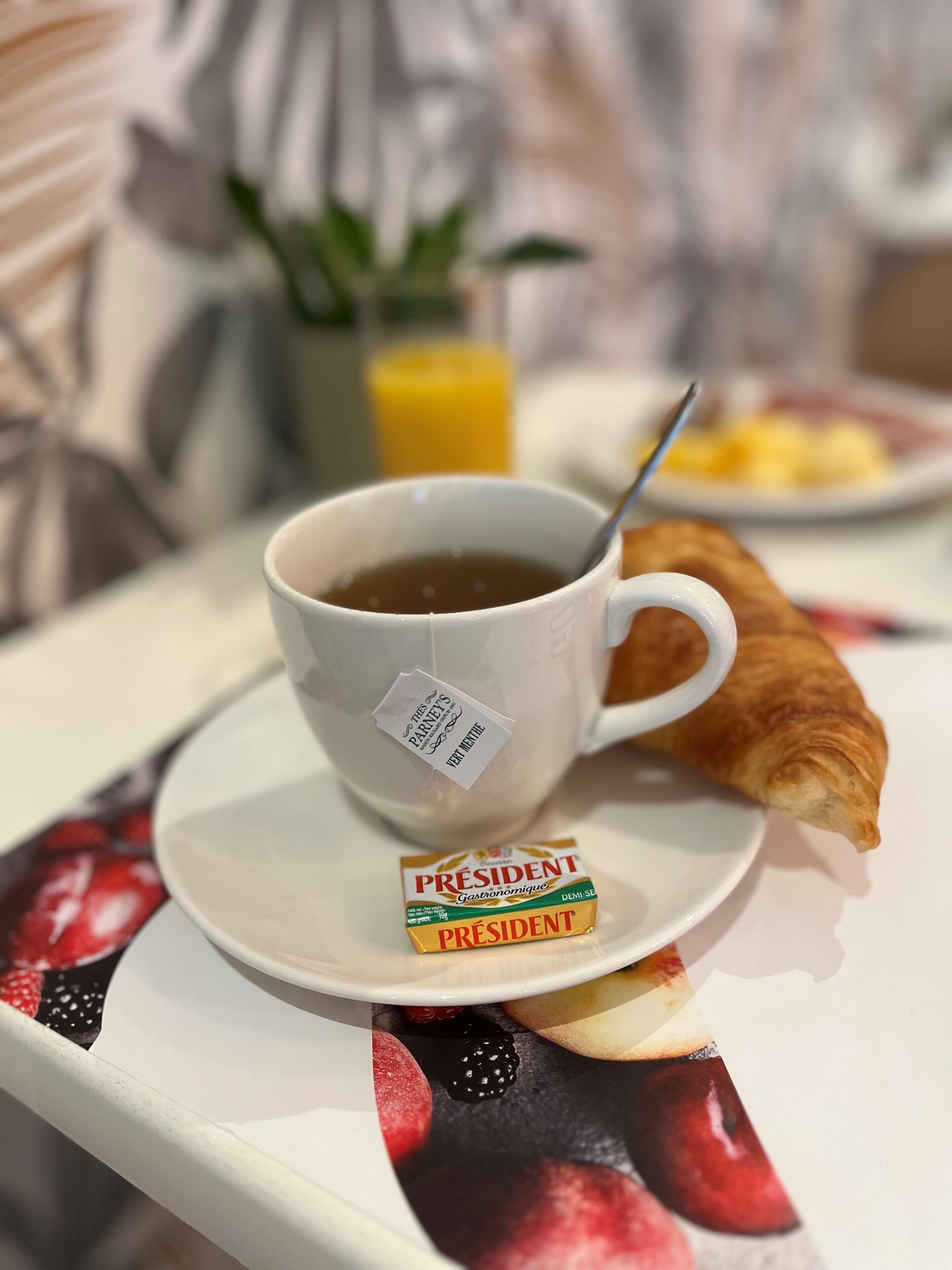 Uma chávena de café com um saquinho de chá, um croissant e uma embalagem de Presidente Gastronomique num tabuleiro.