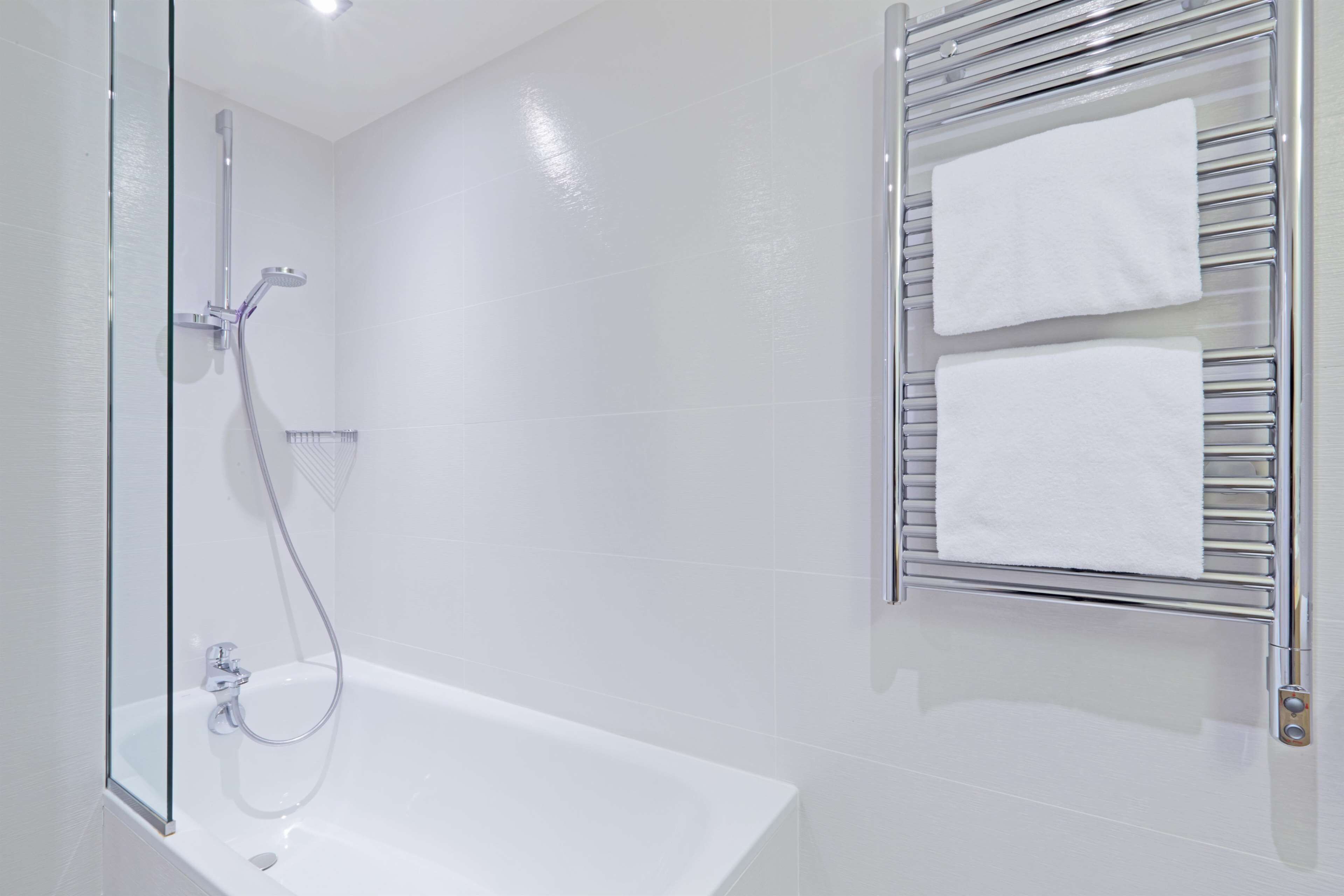 A modern bathroom with a glass-enclosed shower, a white bathtub, and a towel rack with two towels.
