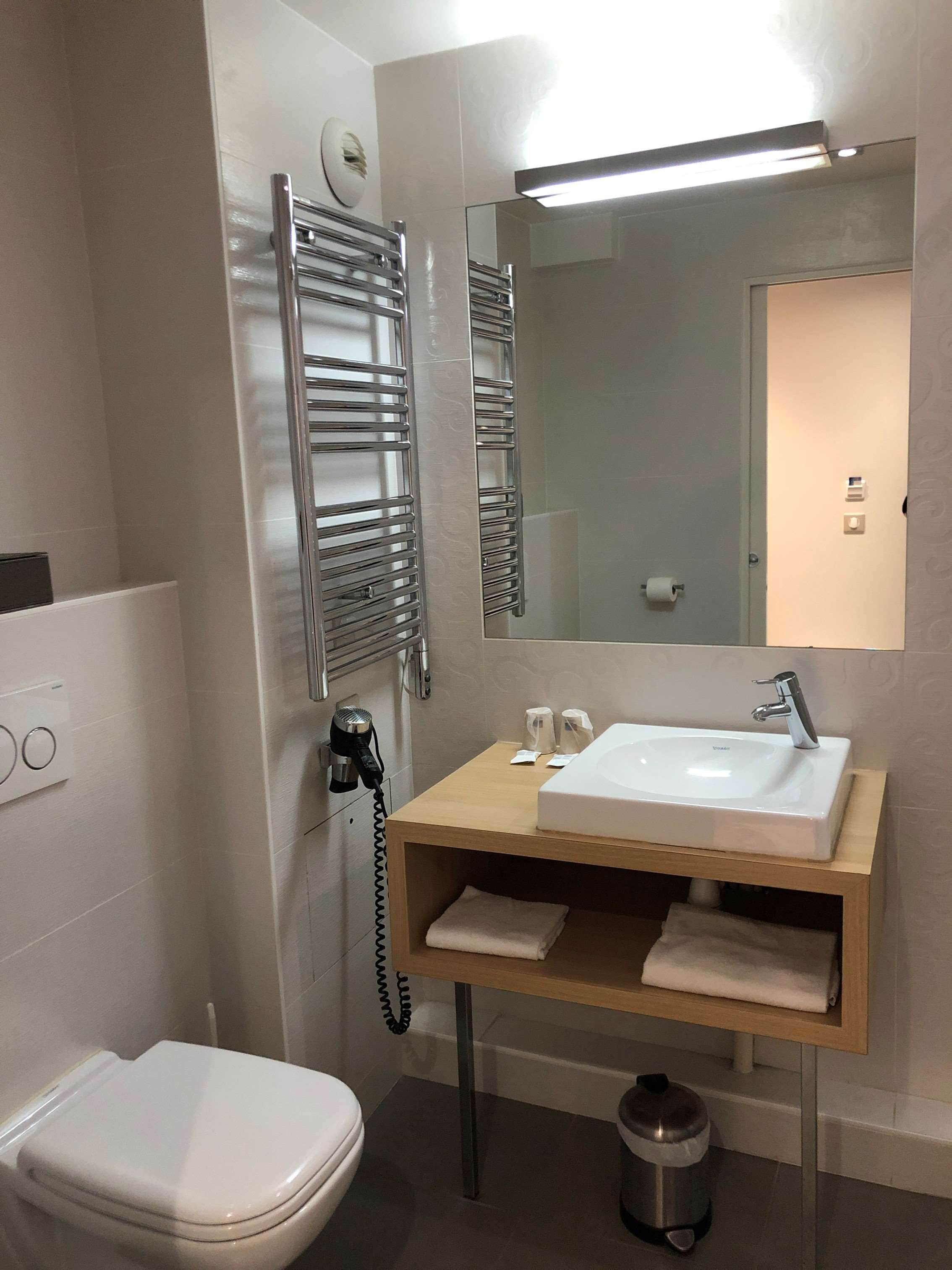 A modern bathroom with a white toilet, a sink with a mirror above it, and a towel rack.