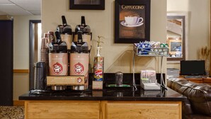 Una estación de café con varias cafeteras, un dispensador de sirope Torani y un cartel enmarcado de cappuccino.