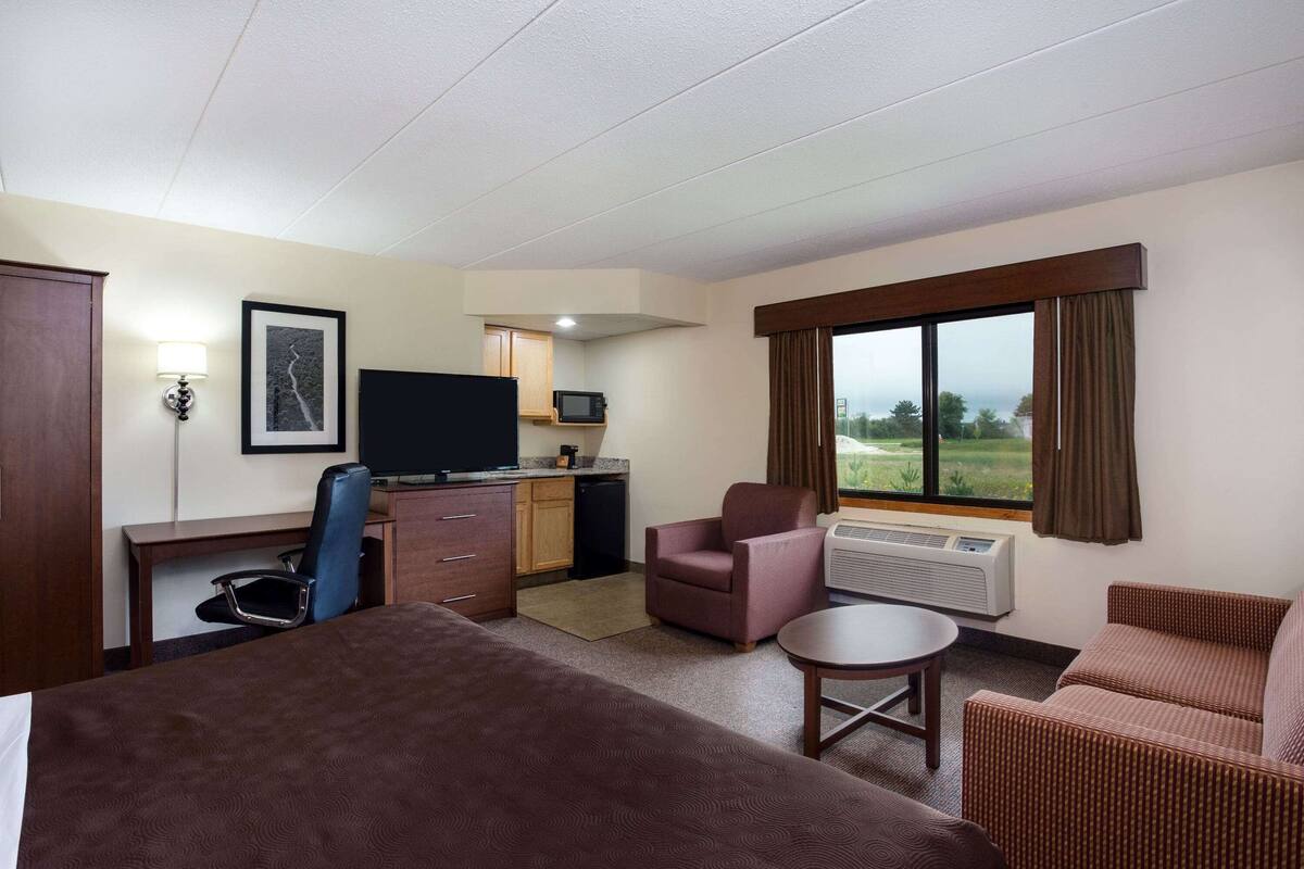 A hotel room with a bed, a desk, a chair, a television, and a view of the outdoors.