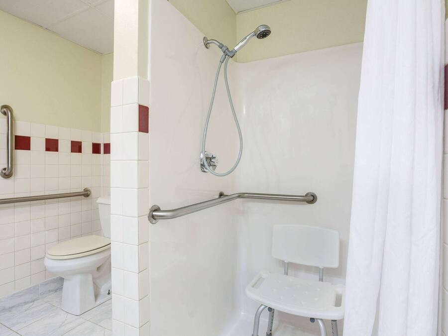 Un baño con inodoro, ducha con barras de apoyo y lavamanos blanco.