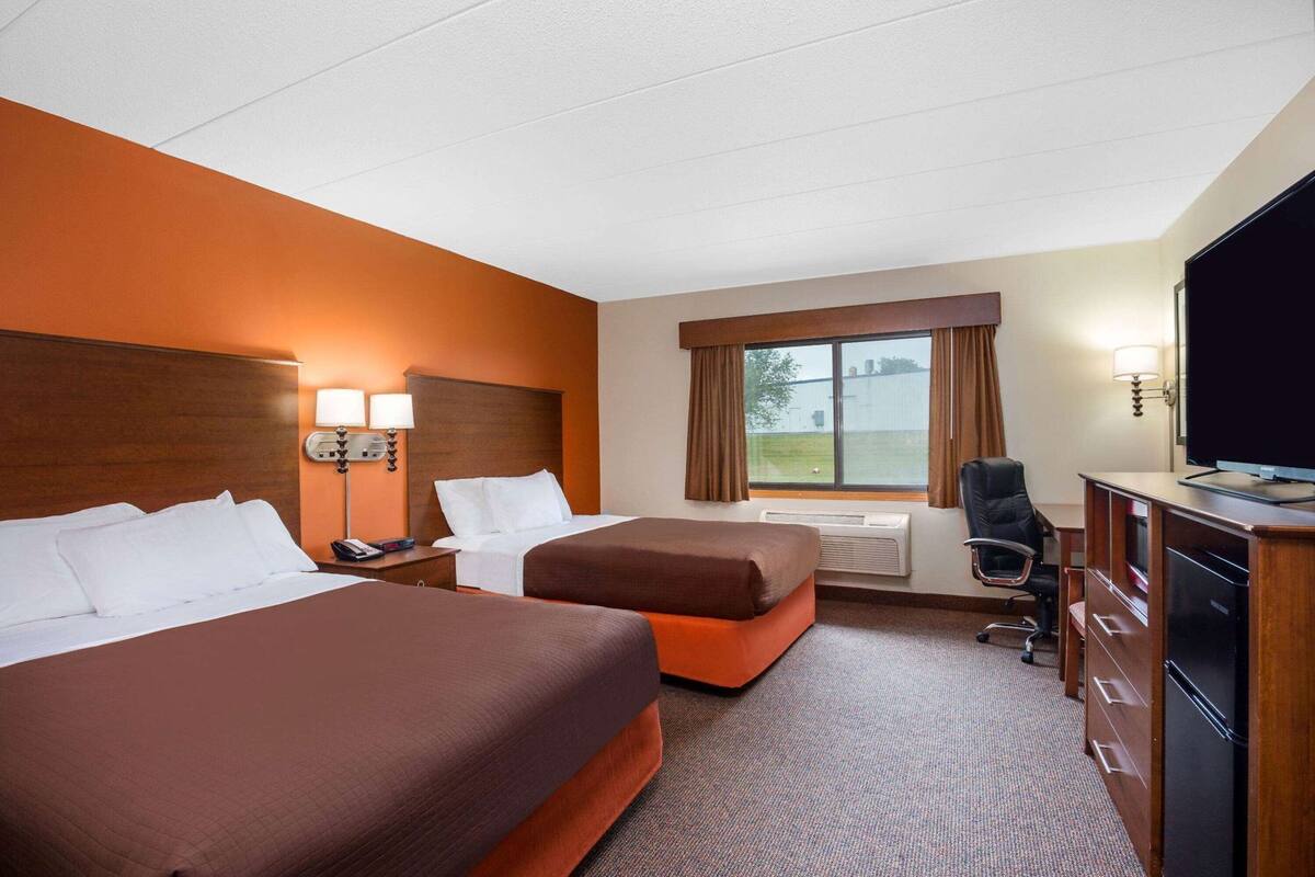 A hotel room with two beds, a desk with a computer, a TV, and a window with curtains.