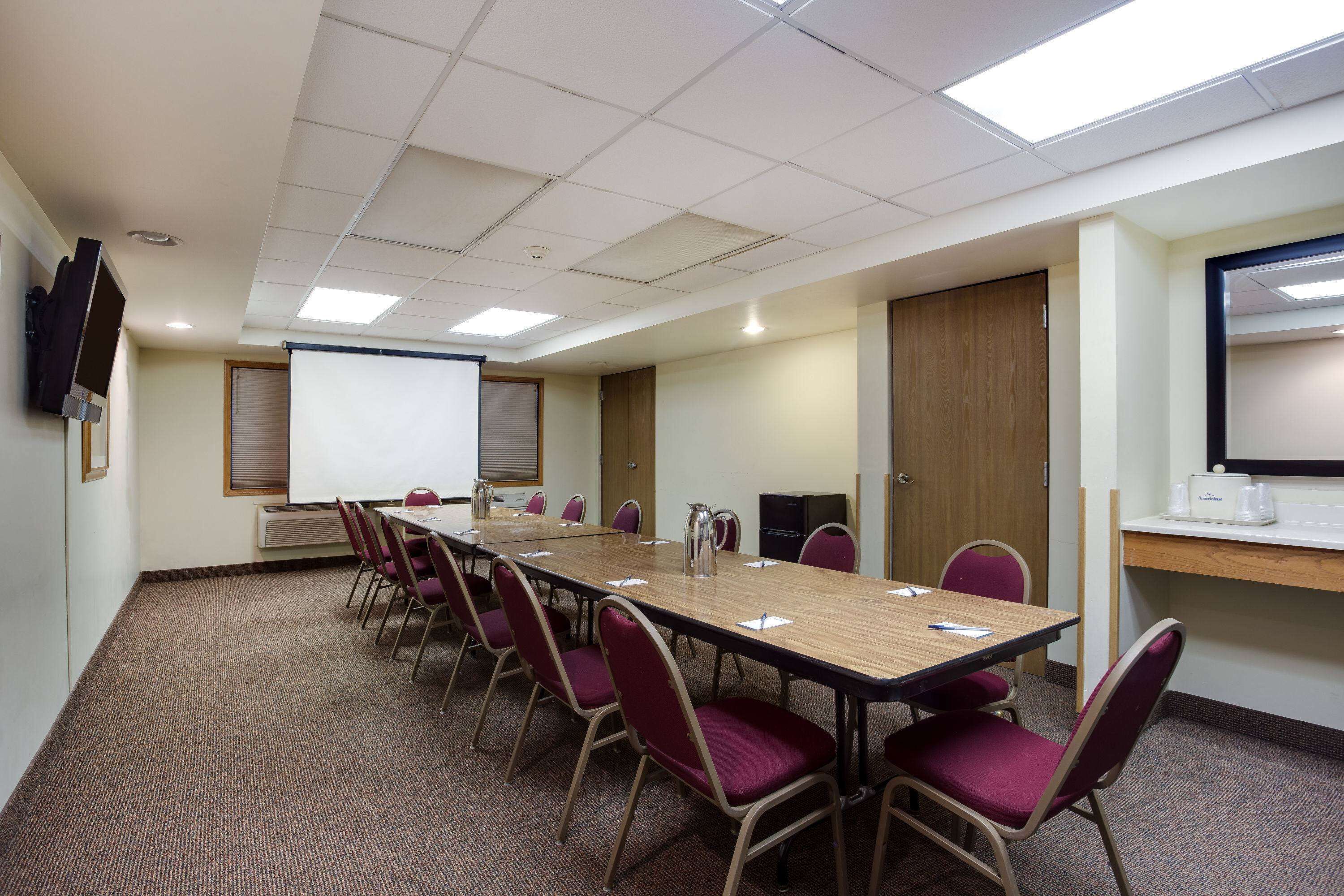 Un salón de conferencias con una larga mesa, sillas, una pantalla de proyector y una pizarra.
