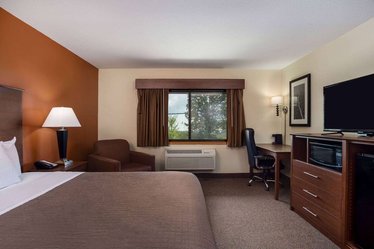 A hotel room with a large bed, a desk with a computer, a chair, a TV, and a window with curtains.
