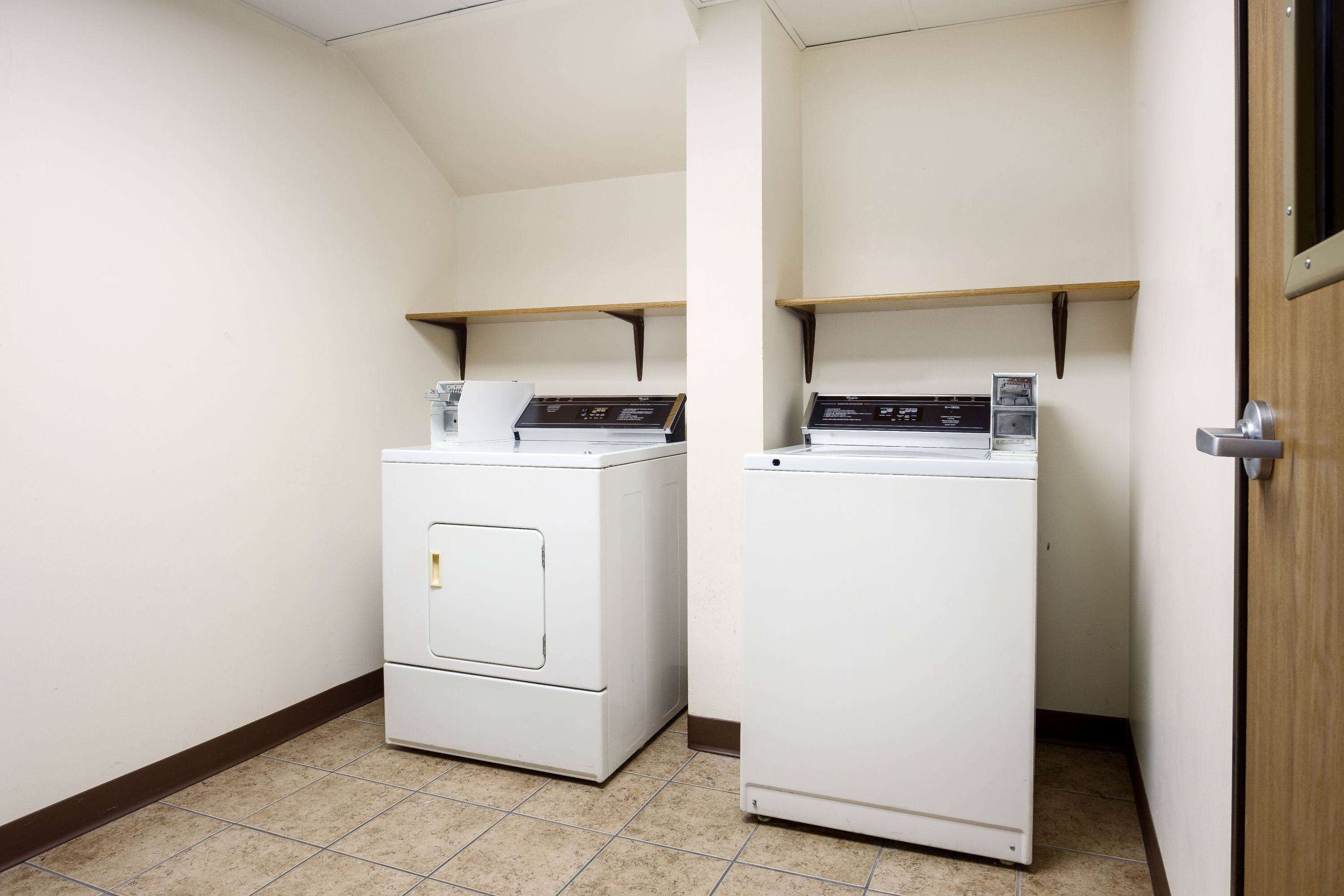 Une buanderie équipée de deux machines à laver et deux sèche-linge superposés, avec des étagères en bois au-dessus et un sol carrelé.