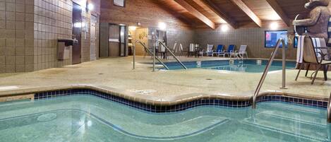 An indoor swimming pool with clear blue water, wooden ceiling beams, and lounge chairs around the pool.