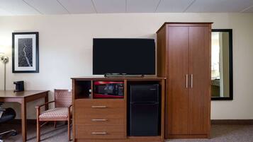 A compact hotel room with a wooden desk, a television, a microwave, a refrigerator, a chair, and a wardrobe.