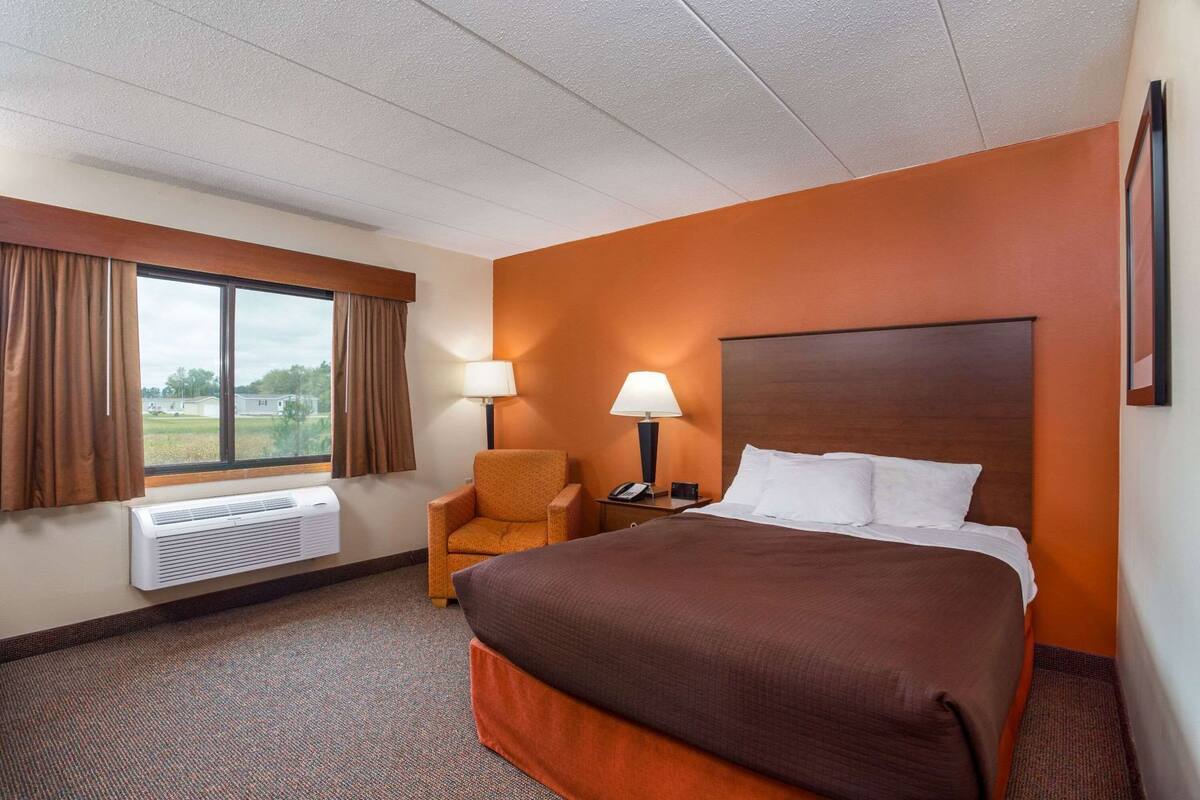 A hotel room with a large bed, a chair, a nightstand with a lamp, and a window with curtains.