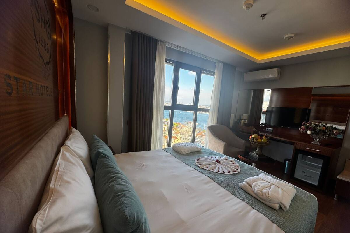 A hotel room with a large bed, a desk, a chair, and a view of the city.