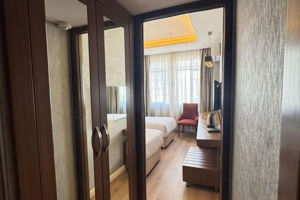 A hotel room with a bed, a desk, a chair, and a window with curtains.