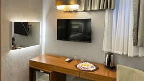 A compact hotel room with a flat-screen TV mounted on the wall, a wooden desk with a laptop, a small fridge, a round table, and a cushioned armchair. - Style Star Hotel Cihangir (Istanbul)
