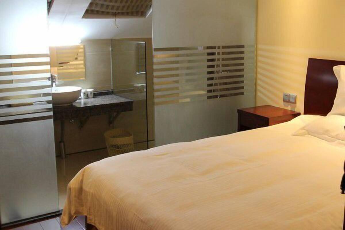 Ein Hotelzimmer mit einem Bett, einem Nachttisch, einem Spiegel und einem Badezimmer mit Waschbecken und Toilette.