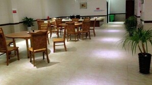 Uma sala de jantar espaçosa com várias mesas e cadeiras de madeira, ventiladores de teto e plantas em vasos.