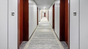 Corredor longo e estreito de um hotel, com portas de madeira e piso coberto de carpete.