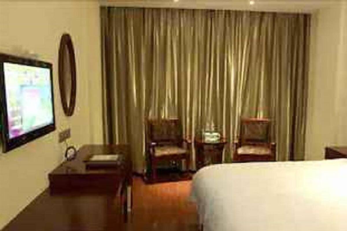 Ein Hotelzimmer mit Bett, Schreibtisch, Stuhl, Fernseher und Vorhang.