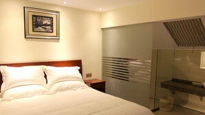 Quarto de hotel com uma cama grande, mesa de cabeceira, quadro na parede, espelho e área de chuveiro.