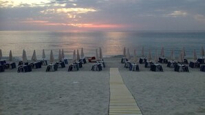 Une plage bordée de rangées de parasols et de chaises longues, toutes orientées vers l’océan.
