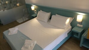 Un lit bien fait, avec du linge de lit blanc et une couvre-lit à motifs bleus, deux tables de chevet avec des lampes, et une chaise en verre transparent.