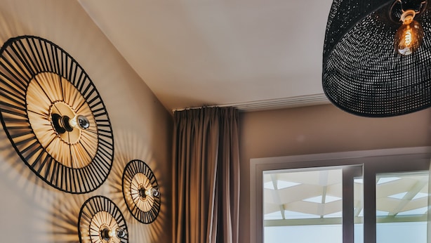 Un salon moderne avec un canapé foncé, des appliques murales décoratives et une vue sur un balcon où se trouve une personne.